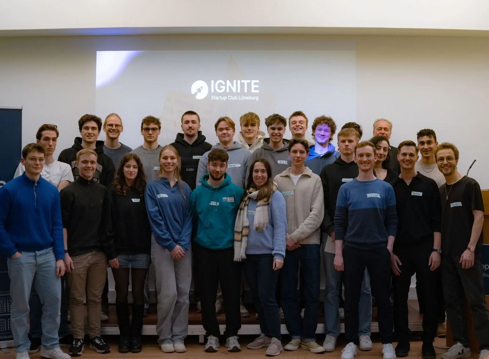 Gruppenfoto vom Kick-off-Event von IGNITE im Utopia: rund 35 Studierende vor der Projektion des IGNITE-Logos.